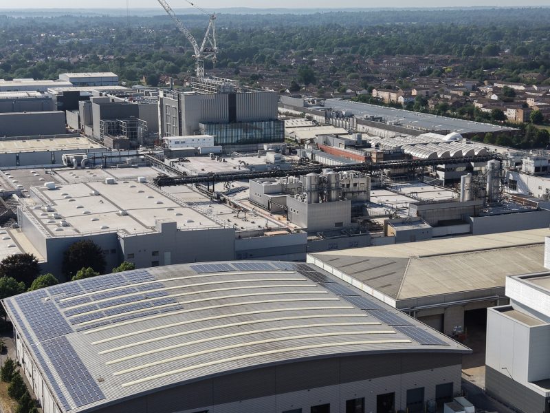 Large data center campus seen from above on a sunny day. Modern buildings contain vital IT infrastructure and processing equipment. Rooftop solar panels generate clean energy.
